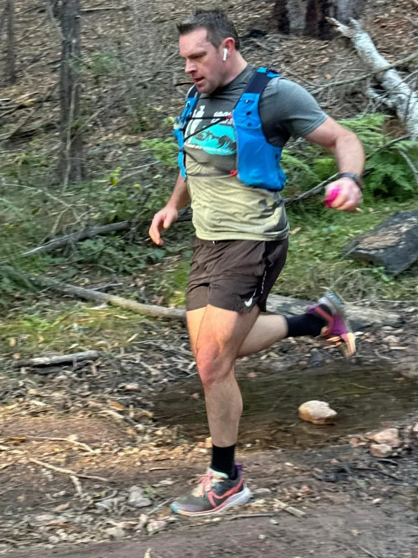 Runner in a hydration vest crossing a rocky creek