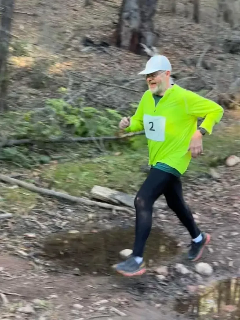 Runner in a high-visibility top stepping across a shallow creek