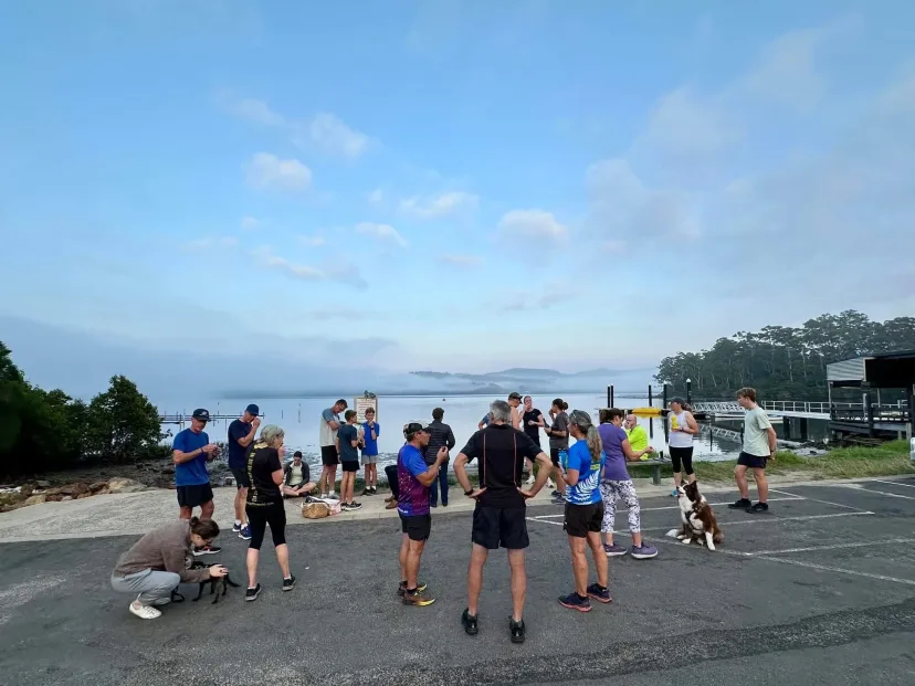 Members and dogs gathered in a waterfront car park at dawn