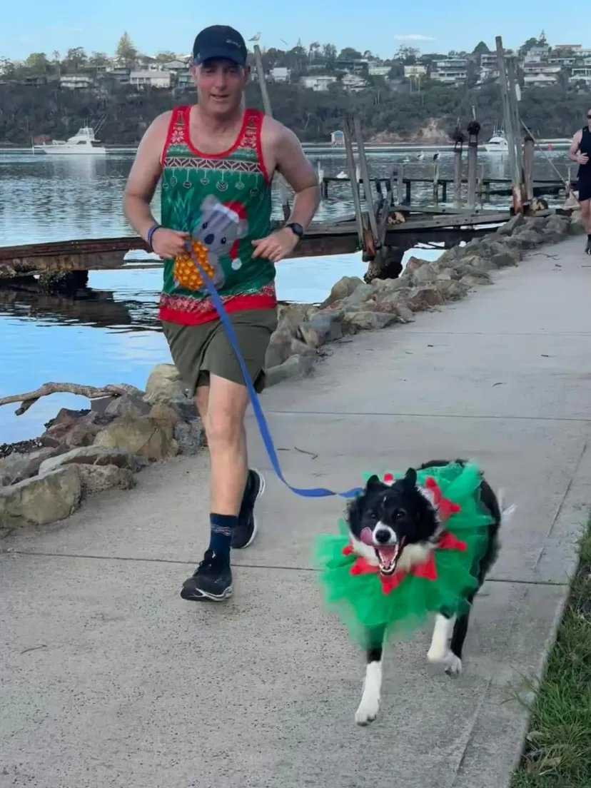 Runner with a dog on a lead on a path beside the water
