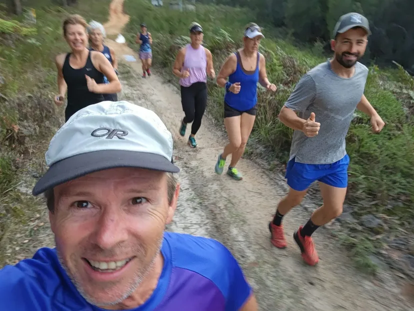 Selfie of a runner with the group running up a hill behind