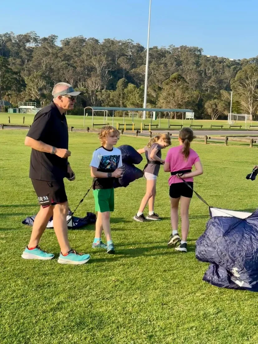 Coach with junior runners on the oval, equipment laid out