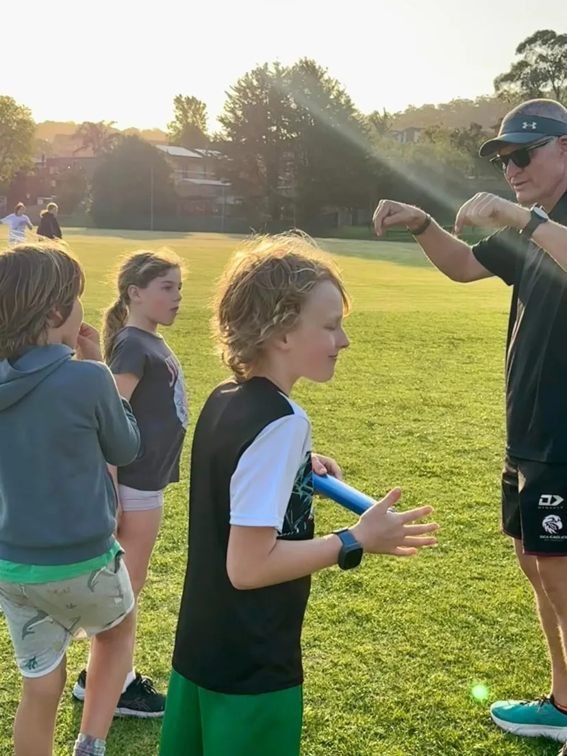 Coach handing out equipment to junior runners on the oval