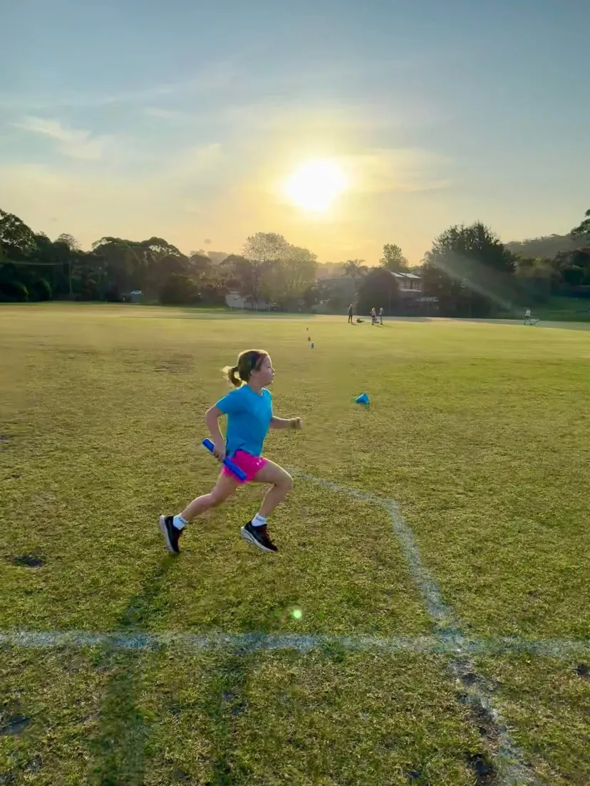 Junior runner running across the oval into the late sun