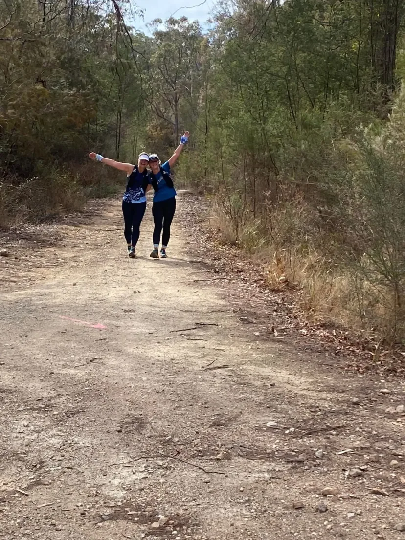 Runner with arms raised on a wide dirt trail through bushland