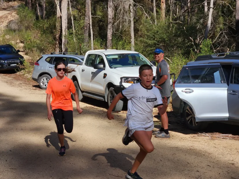 Two runners on a dirt track past parked four wheel drives